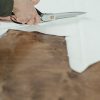 An artisan cuts white fabric on a wooden surface, emphasizing craftsmanship.